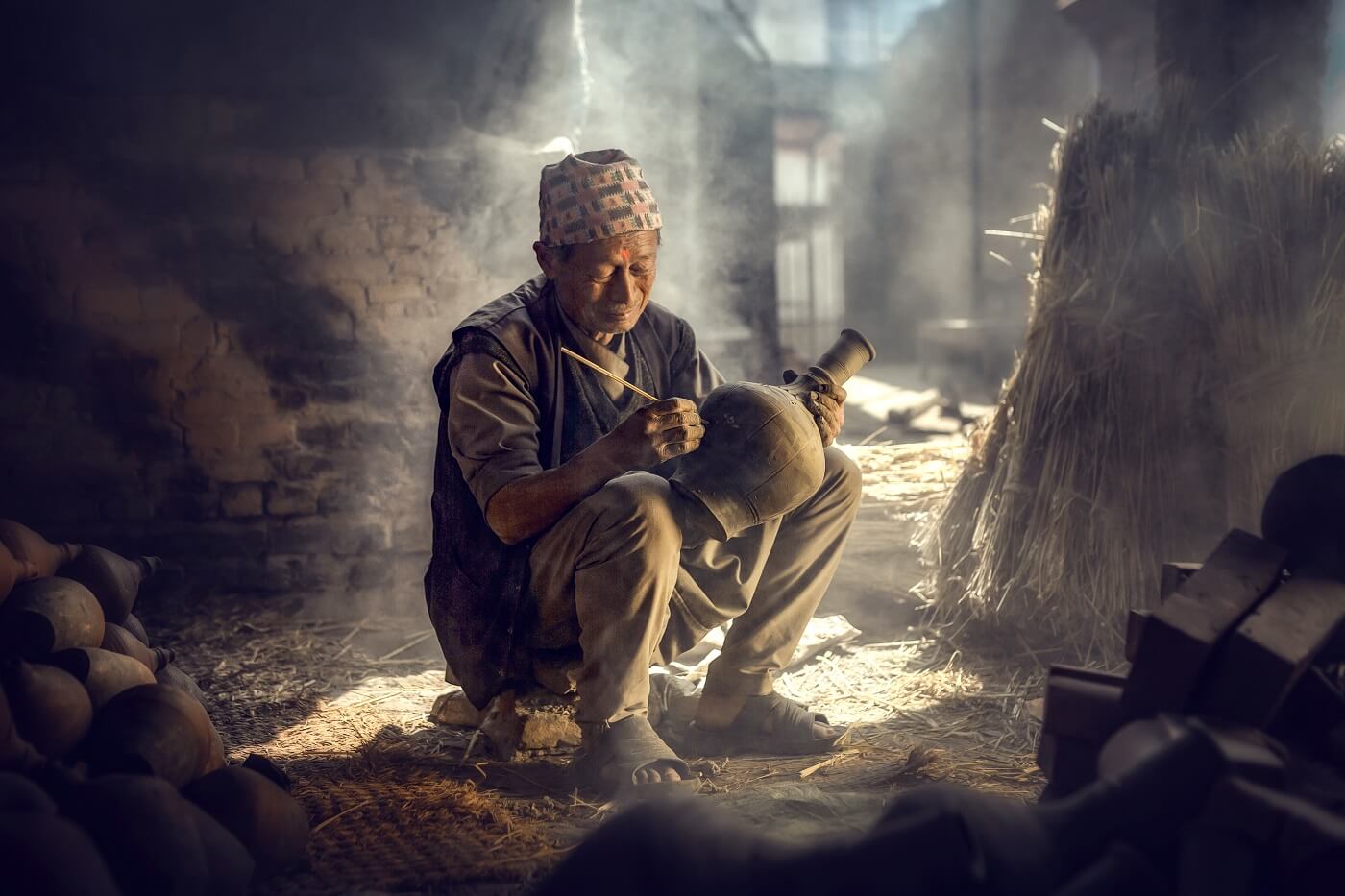 The old man is painting in a clay pot in Durbar square near old hindu temples.